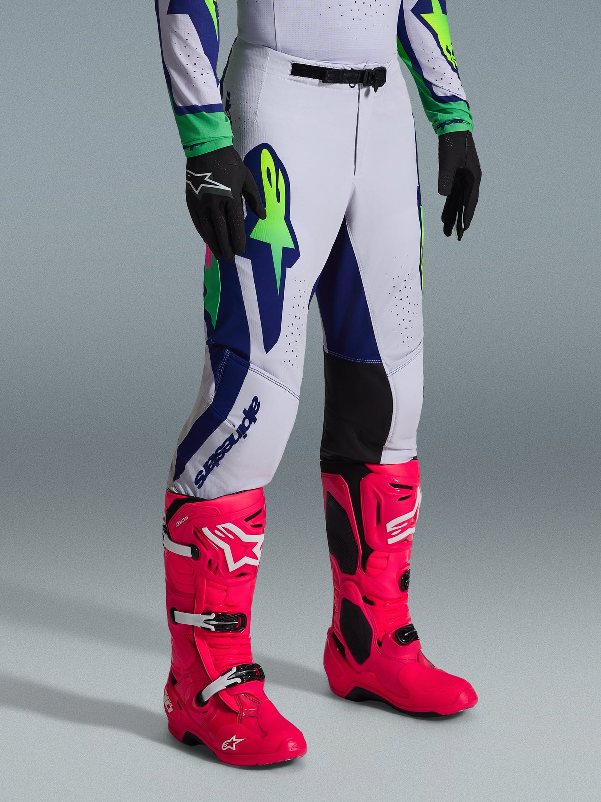 Alpinestars 2026 Supertech Vista Gear Set, pantaloni da motocross, grigio chiaro con accenti blu navy e verde lime, indossati con stivali rosa acceso e guanti neri, vestibilità atletica professionale e grafiche audaci