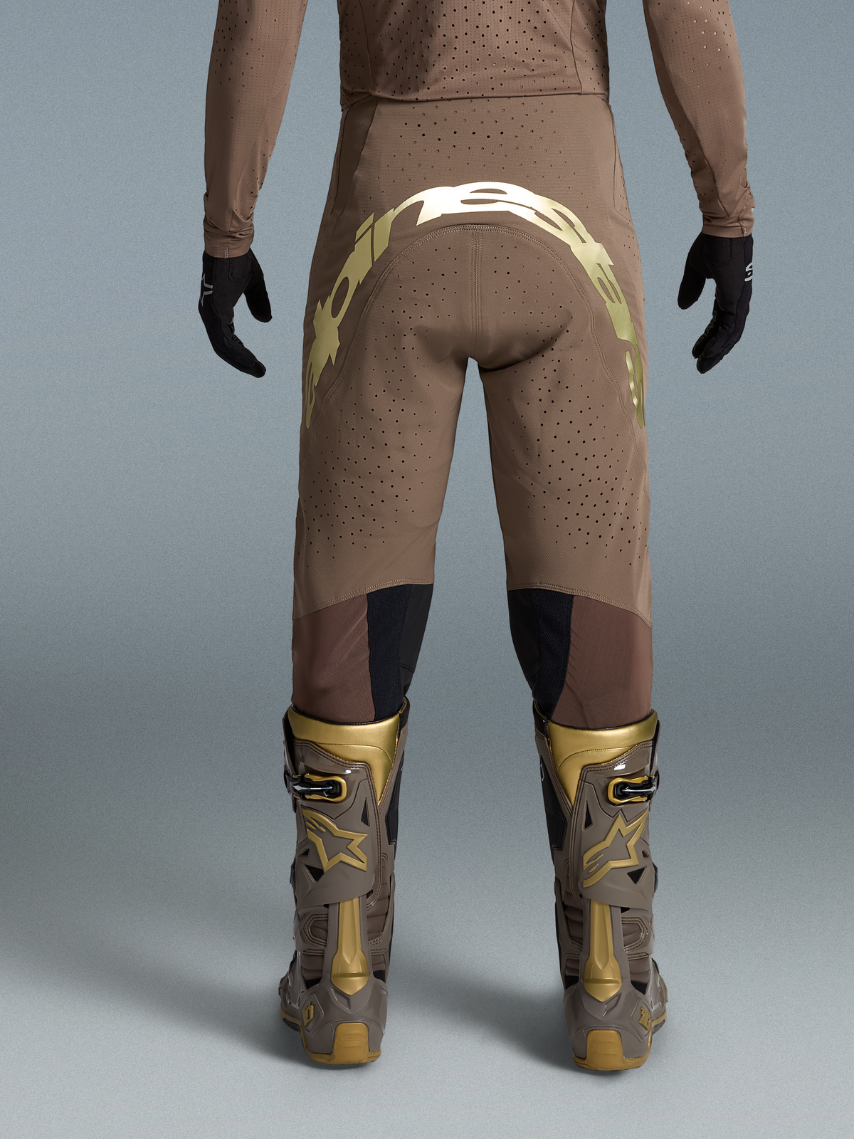 Alpinestars Pantaloni Supertech Air Gold Edizione Limitata, pantaloni da motocross da uomo, marrone e oro, tessuto traforato traspirante, grafica racing posteriore, indossati con stivali Tech 10