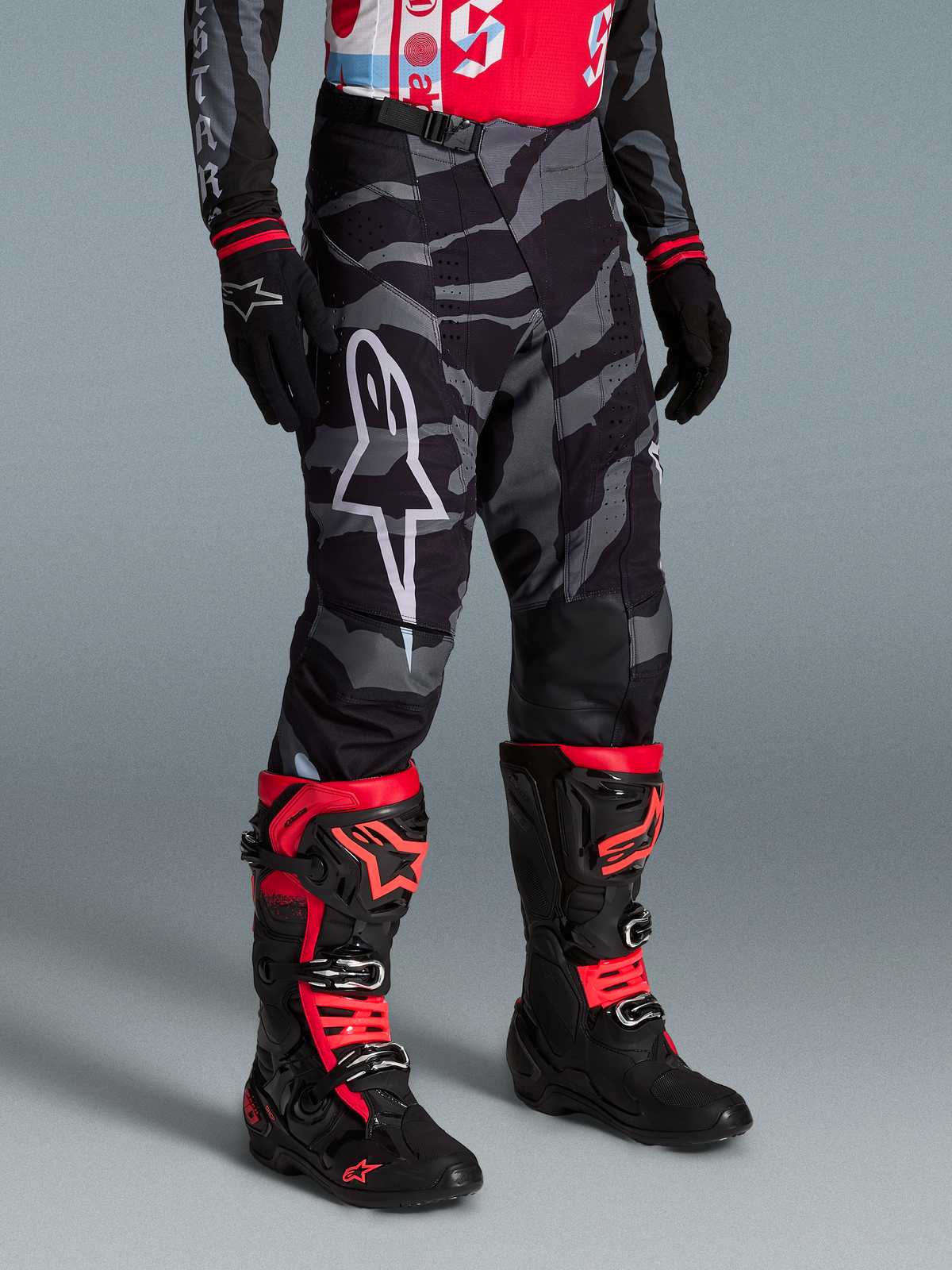 Alpinestars Pantaloni Techstar Beast Coast Edizione Limitata, mimetici neri e grigi con stivali da motocross rossi e neri.