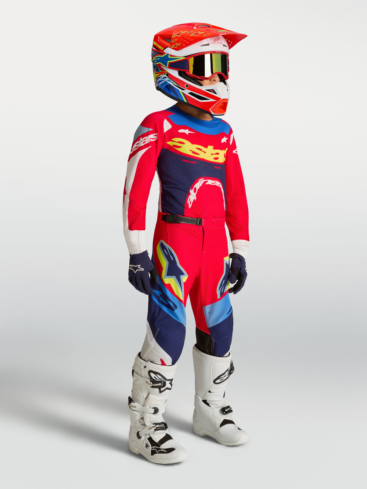 Alpinestars Pantaloni Supertech Dyna Ragazzo, abbigliamento da motocross per ragazzi, rosso e blu navy, indossati con maglia coordinata, casco e stivali bianchi