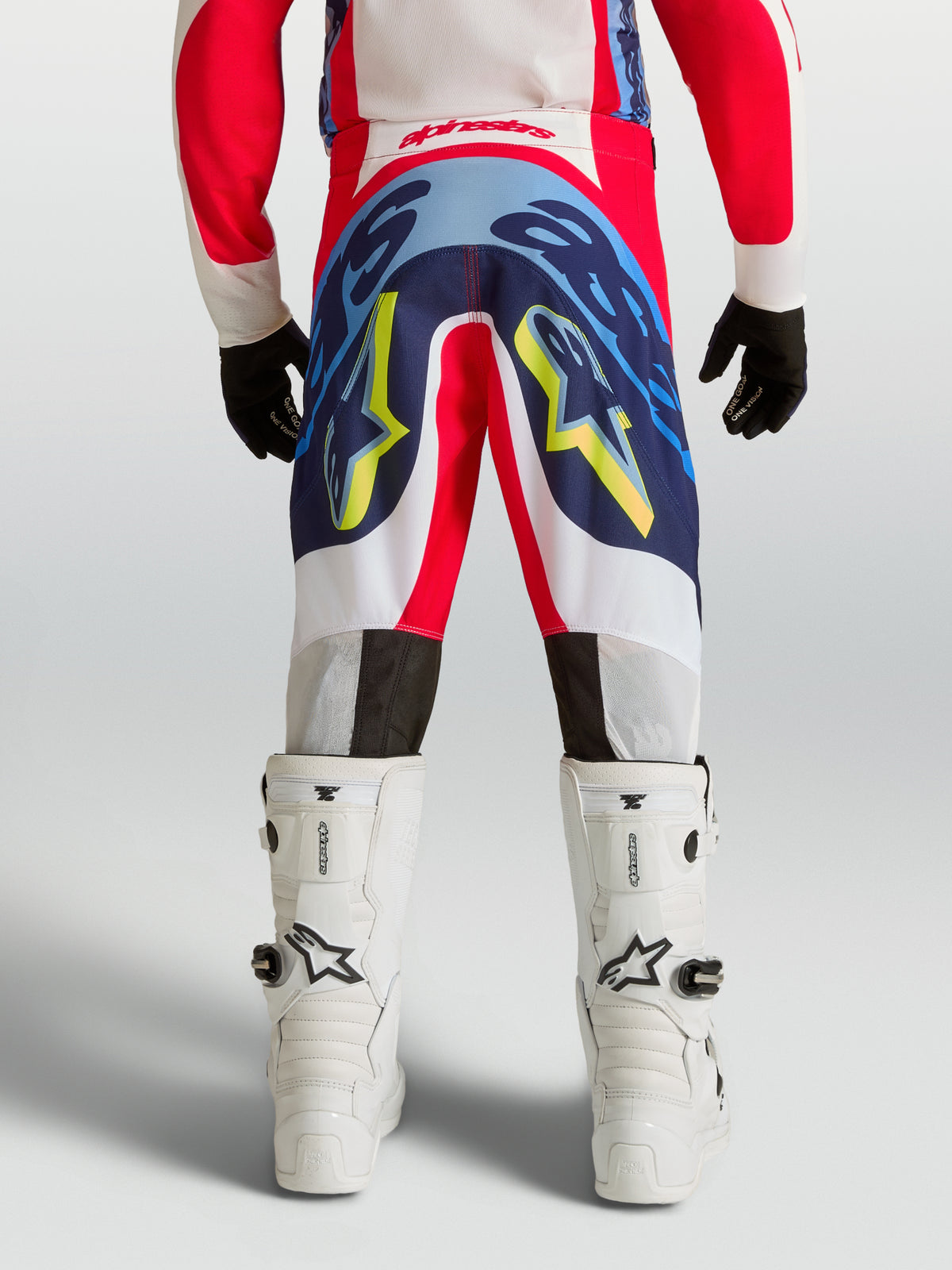 Alpinestars Pantaloni Supertech Dyna Ragazzo, pantaloni da motocross professionali per giovani piloti, rosso e blu navy, costruzione rip-stop elasticizzata, vista posteriore su modello con stivali bianchi, abbigliamento tecnico per gare off-road