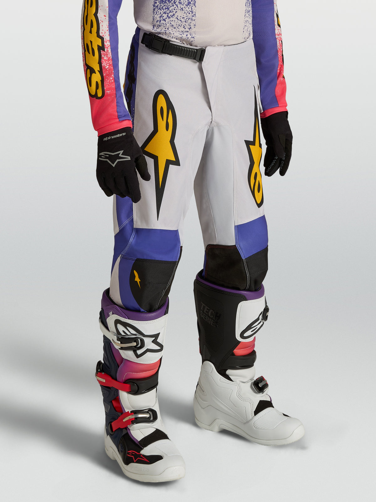 Alpinestars Pantaloni Fluid Drag Ragazzo, pantaloni da motocross bianchi, blu e viola con grafiche oro e design precurvato.