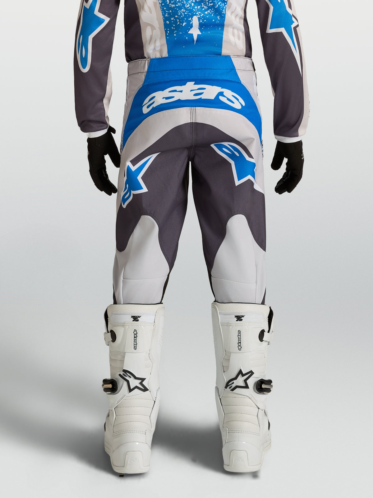 Alpinestars Pantaloni Fluid Drag Ragazzo 2027, pantaloni da motocross blu e grigi, vestibilità precurvata, vista posteriore con stivali bianchi, abbigliamento tecnico off-road.