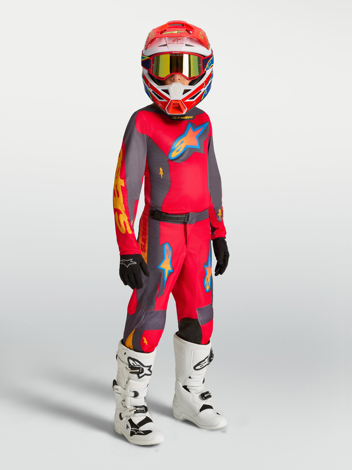 Alpinestars Pantaloni Fluid Hunt Ragazzo, abbigliamento da motocross rosso e grigio con maglia coordinata e stivali bianchi.