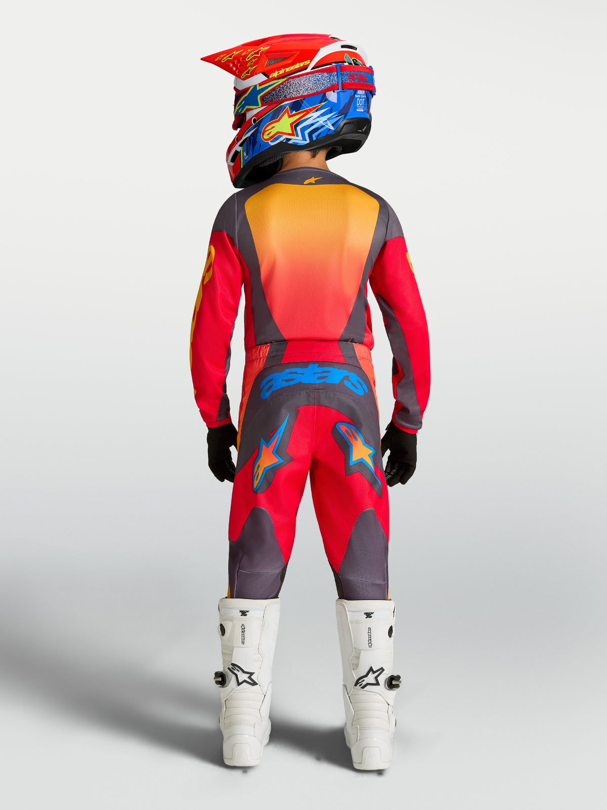 Alpinestars Pantaloni Fluid Hunt Ragazzo 2027, pantaloni da motocross rossi e grigi, vista posteriore di un pilota in attrezzatura completa con stivali bianchi