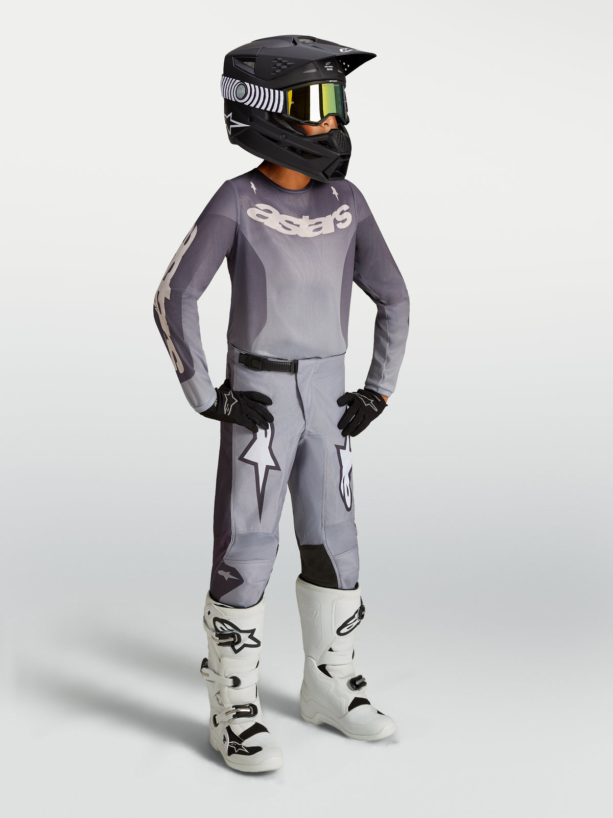 Alpinestars Pantaloni Fluid Amber Ragazzo 2027, pantaloni da motocross per ragazzi, colore sabbia e grigio con grafiche a stella bianche, vestibilità sportiva pre-curvata, rinforzati per off-road, indossati con casco nero e stivali bianchi