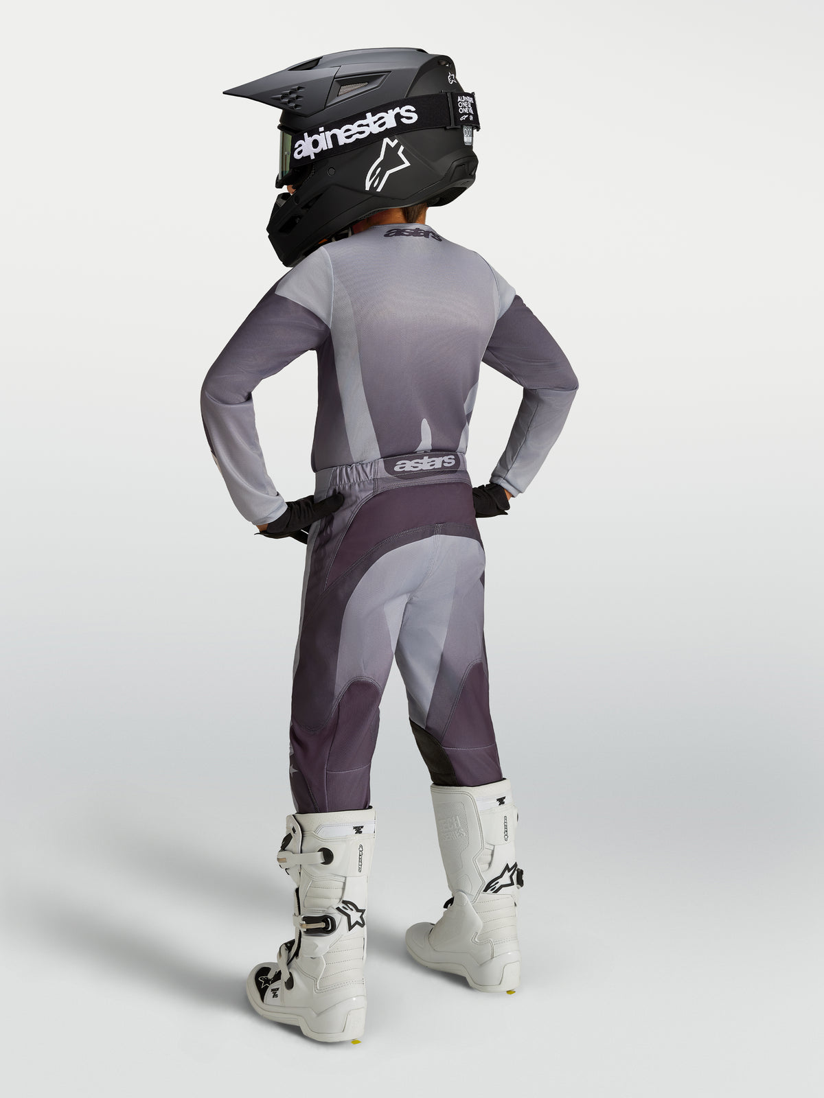 Alpinestars Pantaloni Fluid Amber Ragazzo, pantaloni da motocross grigi e viola, vestibilità sportiva per fuoristrada, mostrati con stivali da moto bianchi.