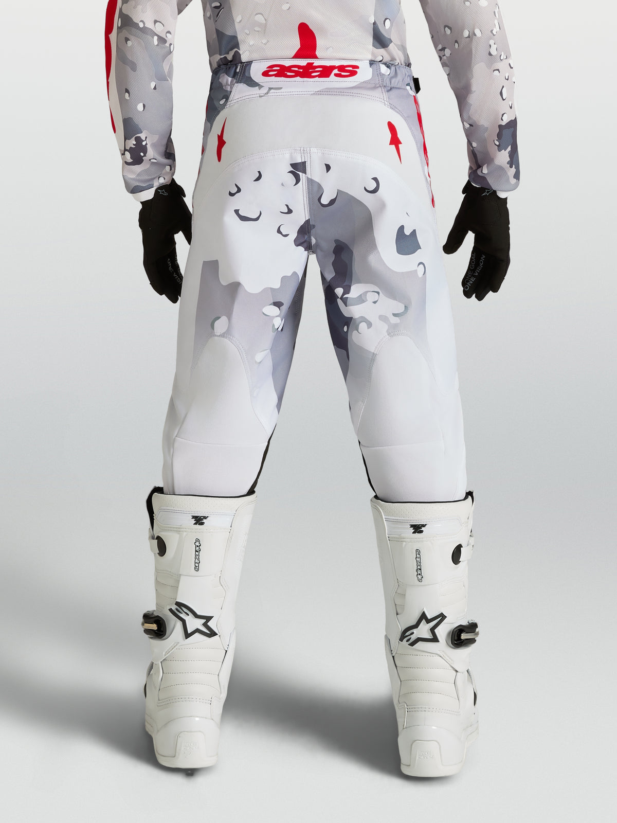 Alpinestars Pantaloni Fluid Lone Ragazzo, pantaloni da motocross per ragazzi, grigio camouflage e bianchi con dettagli rossi, vista posteriore su pilota.