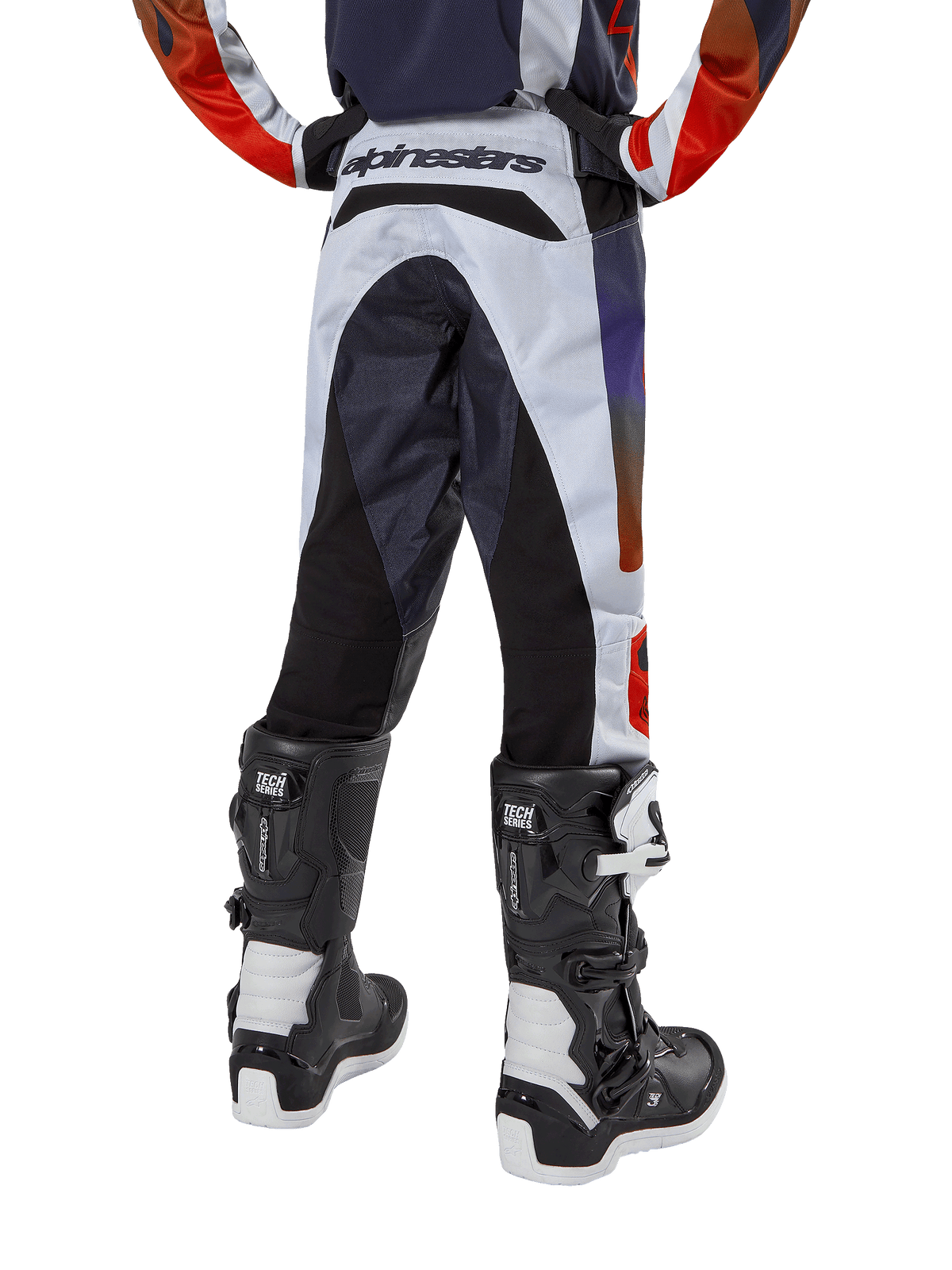Alpinestars pantaloni Youth 2024 Racer Hoen, pantaloni da motocross, grigio chiaro con accenti arancione acceso e nero, vista posteriore con pannelli neri sulla seduta e sulle gambe, branding evidente sulla vita posteriore, indossati con stivali da motocross bianchi e neri per corse fuoristrada