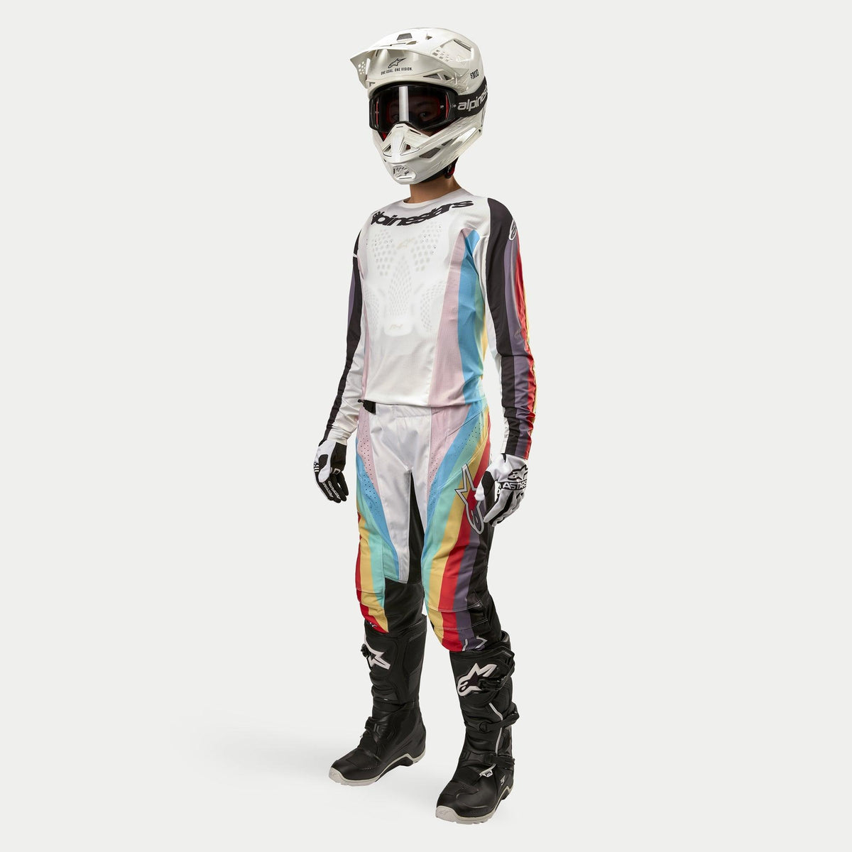 Pilota di motocross che indossa pantaloni Alpinestars Stella Techstar 2024 da donna, pantaloni da motocross, Nero Multicolore con pannelli bianchi e vivaci strisce diagonali, maglia coordinata, casco bianco e stivali neri, completo da gara fuoristrada coordinato per donna