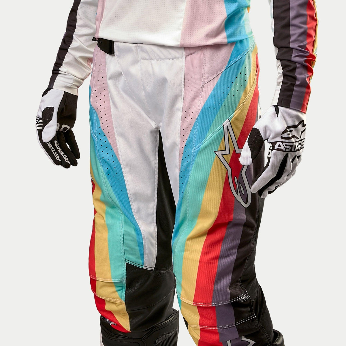 Alpinestars Stella Techstar Pants 2024 da donna, pantaloni da motocross, nero multicolore con vivaci strisce diagonali blu, rosa, giallo e rosso, con un grande logo a stella sulla coscia, indossati con maglia e guanti coordinati, abbigliamento professionale per corse fuoristrada