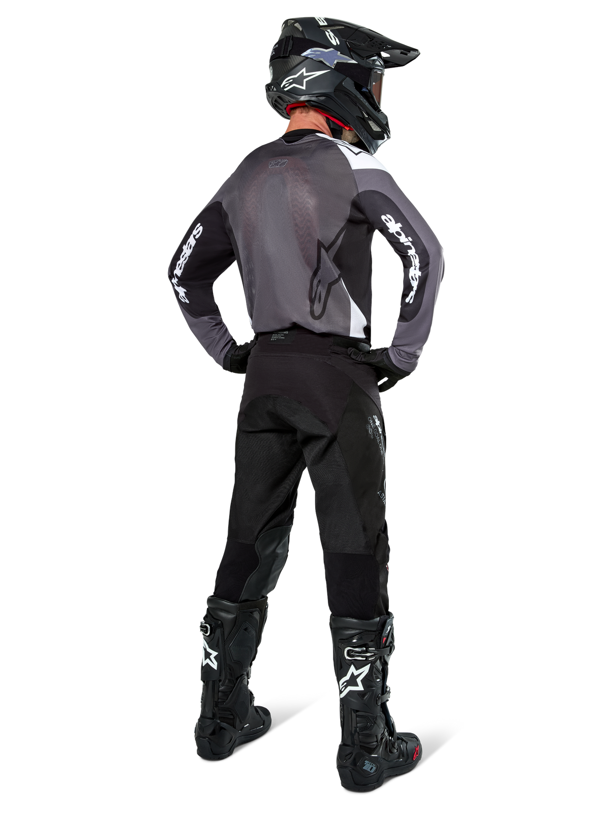 Pilota di motocross con maglia Alpinestars Pro-Dura in Black Magnet White, vista posteriore con pannello in mesh grigio e maniche nere con marchio Alpinestars bianco, coordinata con pantaloni neri, casco nero e stivali neri e bianchi, equipaggiamento professionale da enduro
