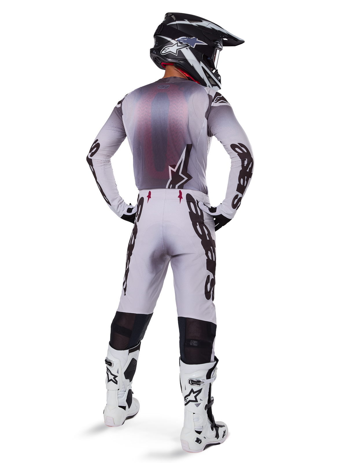 Pilota di motocross con abbigliamento da gara completo, maglia grigia e nera, pantaloni grigio chiaro con marchio 'Astars' nero sui lati, casco nero e bianco, stivali Tech 10 bianchi, completo professionale da gara off-road coordinato