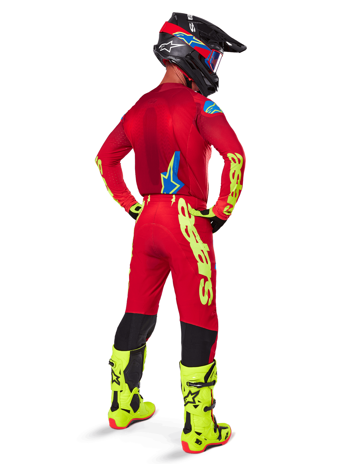 Pilota di motocross visto di spalle che indossa la maglia Alpinestars 2025 Supertech Maker, rosso acceso e giallo fluo, pantaloni coordinati con loghi gialli, stivali giallo fluo e casco nero e rosso, outfit coordinato per corse off-road di livello professionale