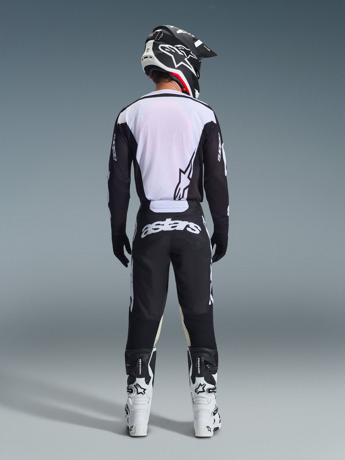 Set completo Alpinestars Racer Air Riway 2026, abbigliamento da motocross, nero e bianco, vista posteriore del pilota con maglia ventilata a pannelli in mesh bianchi, pantaloni coordinati con logo astars sulla seduta, abbinato a stivali e casco bianchi e neri