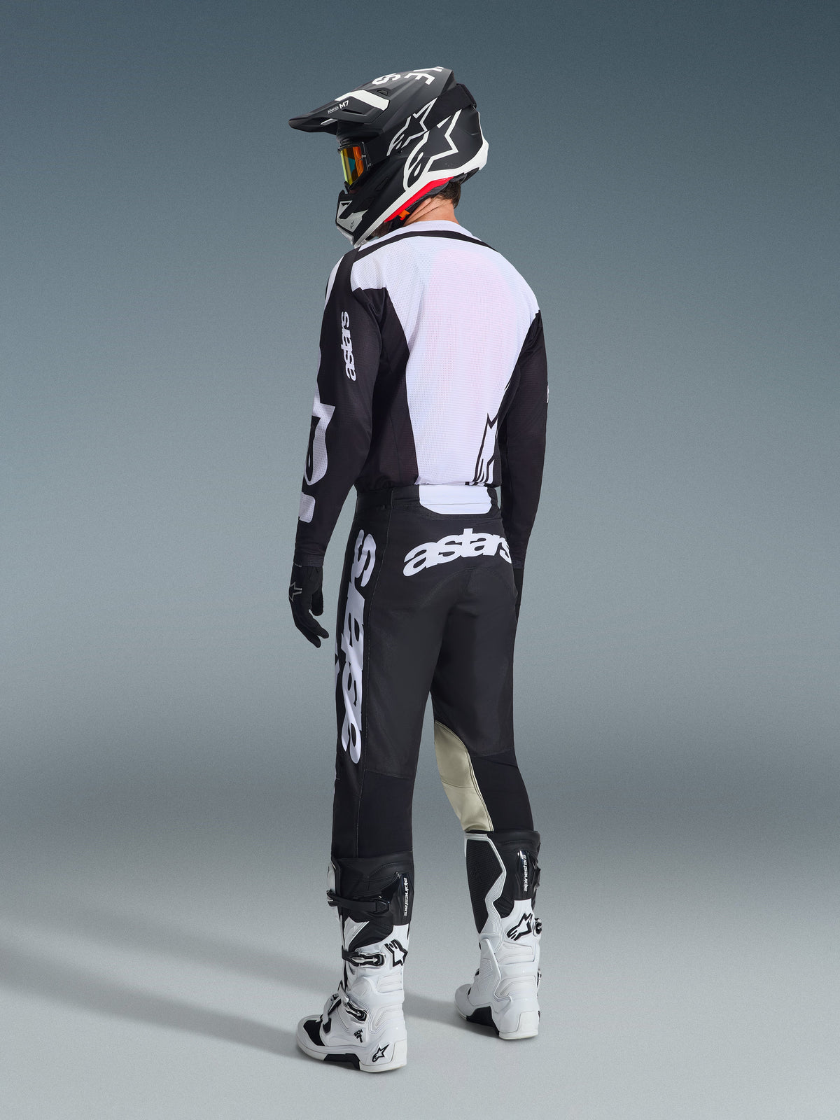 Pilota di motocross visto da dietro con il completo Alpinestars 2026 Racer Air Riway in nero e bianco, maglia con schiena in mesh ventilato e grandi loghi bianchi, abbinato a un casco nero e stivali bianchi.