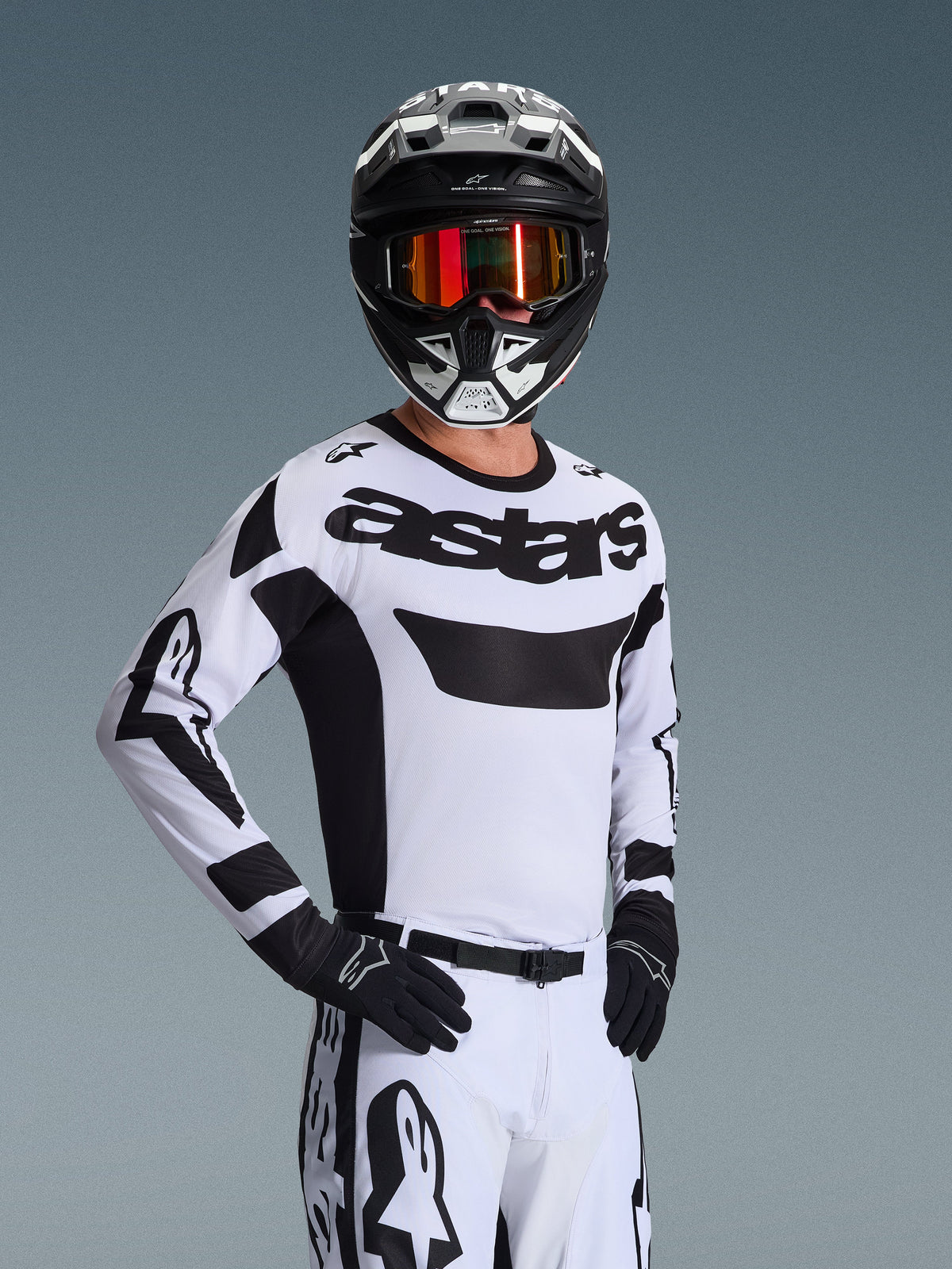 Maglia Alpinestars Racer Riway 2026, maglia da motocross, bianco e nero, con logo 'astars' evidente sul petto, indossata con pantaloni bianchi coordinati e guanti neri, casco bianco e nero con maschera rossa riflettente, abbigliamento professionale per corse fuoristrada