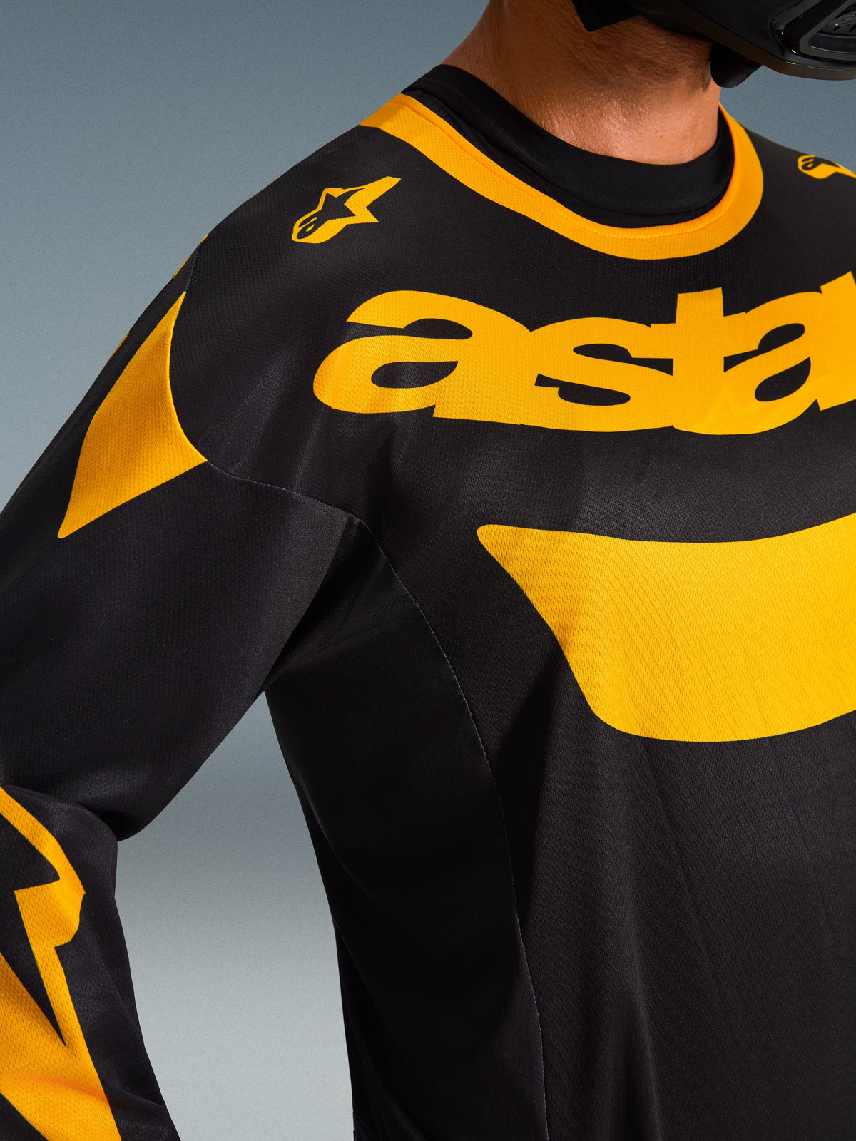 Primo piano della maglia Alpinestars Racer Riway 2026, nero e giallo, con audace logo giallo sul petto, costruzione in tessuto mesh tecnico per la ventilazione, abbigliamento da motocross ad alte prestazioni