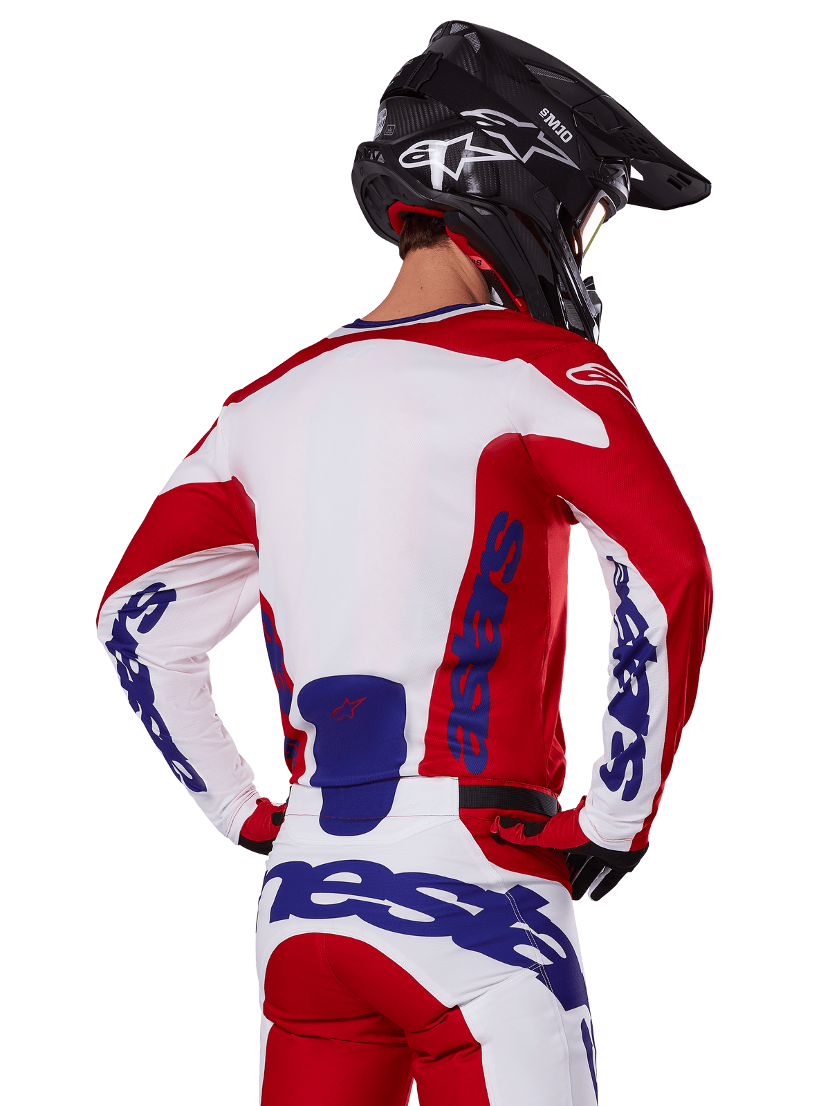 Maglia e pantaloni Alpinestars Racer Veil 2025, completo da motocross, rosso acceso, bianco e blu, vista posteriore del pilota che indossa il completo coordinato e un casco da motocross nero, con branding Alpinestars blu in evidenza, abbigliamento tecnico da corsa off-road
