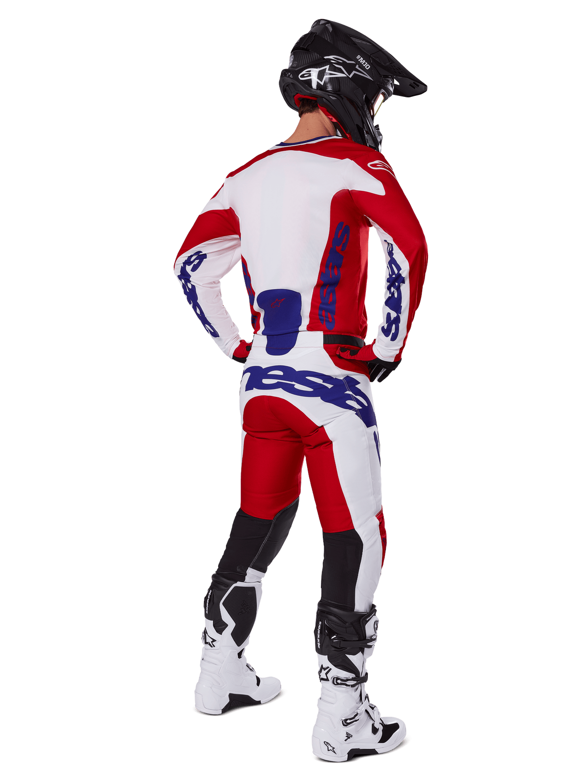 Pilota di motocross visto da dietro che indossa la maglia e i pantaloni Alpinestars Racer Veil 2025 in rosso e bianco, con loghi blu, casco nero e stivali bianchi, set completo di abbigliamento per corse fuoristrada