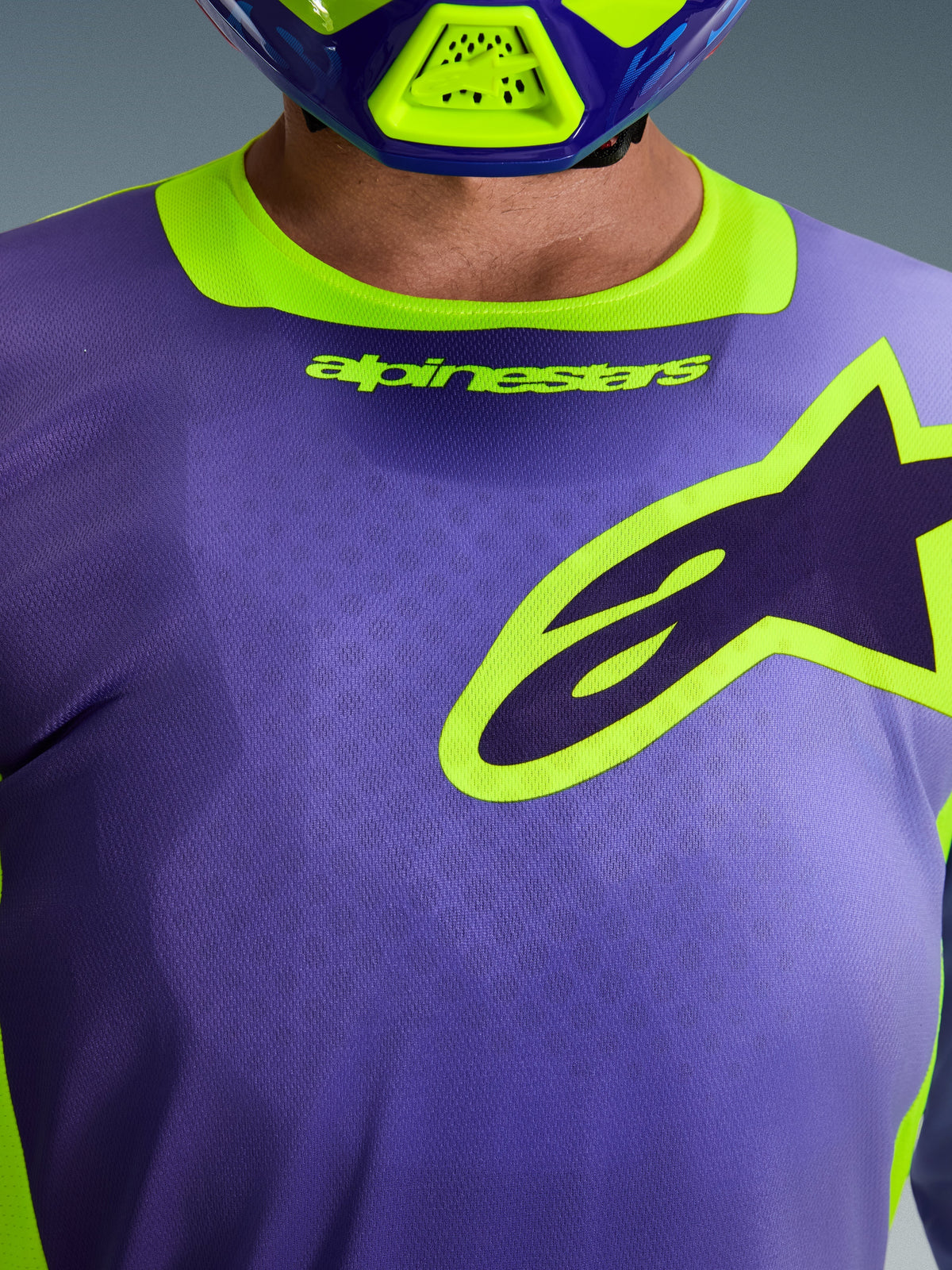 Maglia Alpinestars Racer Portl 2026, viola e giallo fluo, primo piano dell'area del petto e del colletto con marchio Alpinestars e logo a stella, indossata con casco da motocross coordinato, abbigliamento tecnico da fuoristrada.