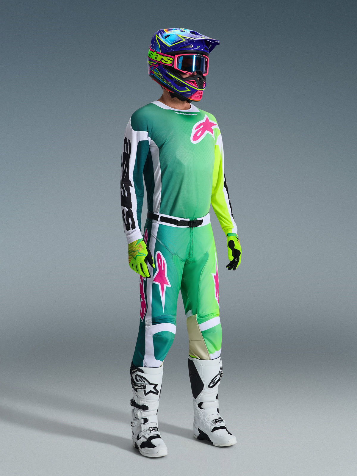 Pilota di motocross con attrezzatura completa, maglia Racer Portl 2026 verde con maniche bianche e nere e logo rosa, pantaloni verdi coordinati con accenti rosa, casco multicolore con maschera, stivali bianchi e neri e guanti verdi, completo coordinato per il fuoristrada