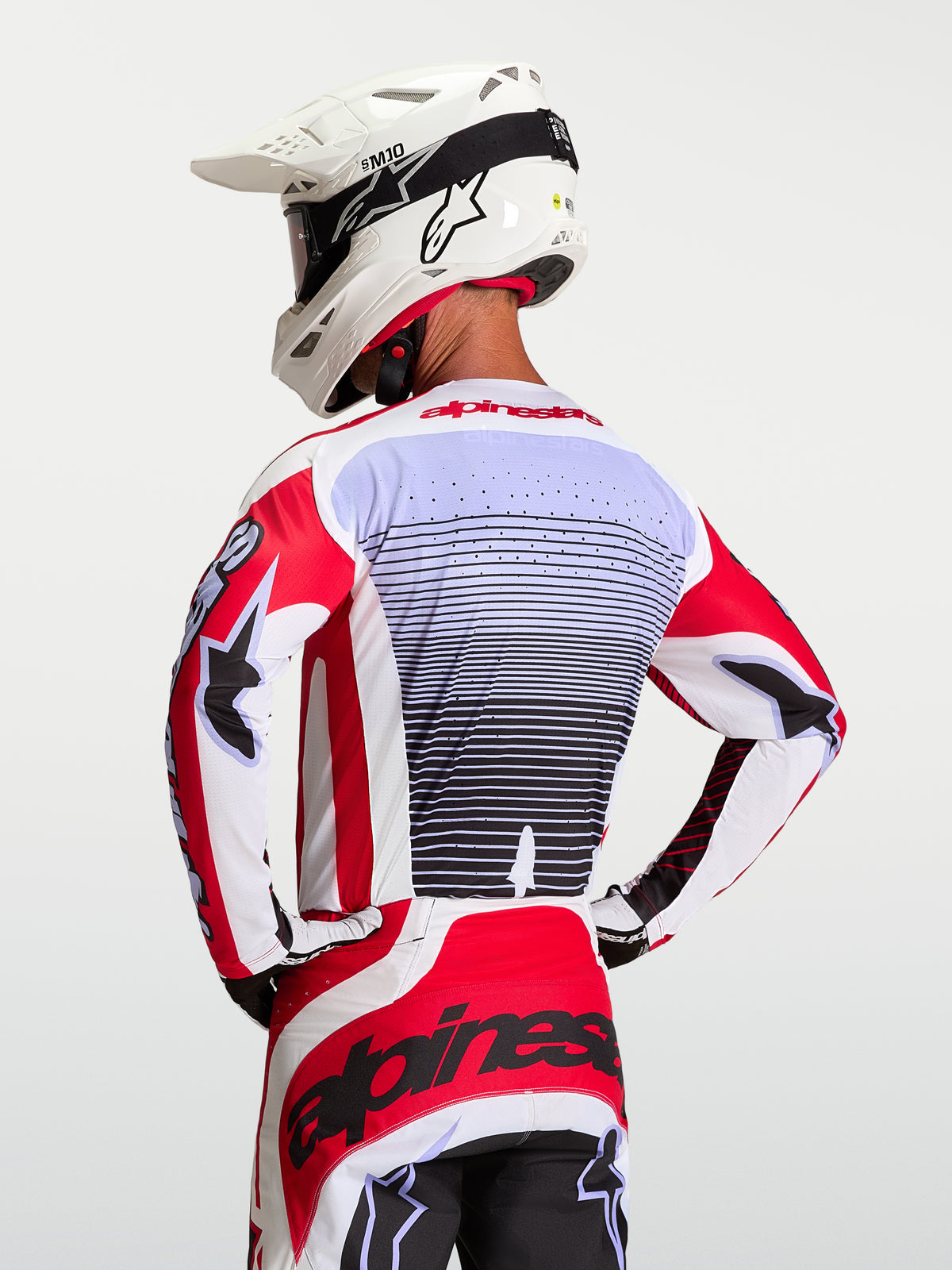 Maglia Alpinestars Techstar Maven, maglia da motocross da uomo, rossa e bianca, traspirante e ventilata, vista posteriore su modello con casco bianco