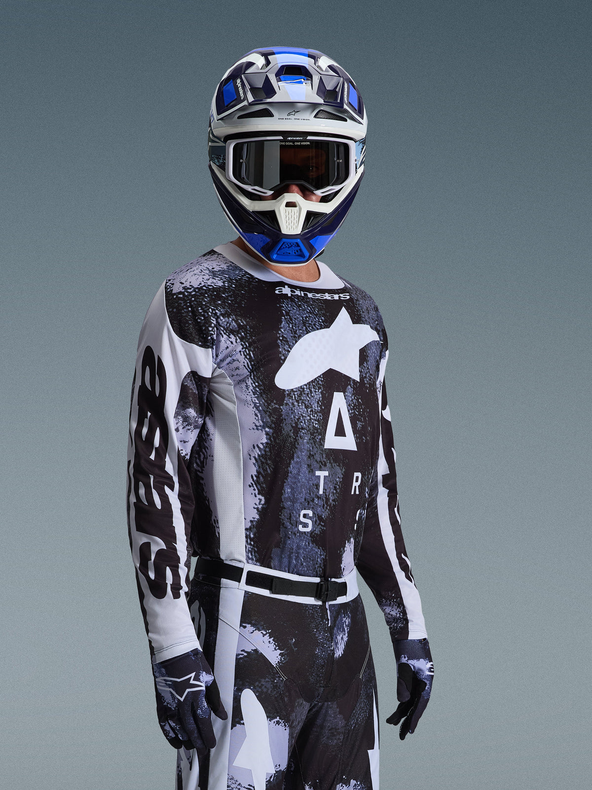 Pilota di motocross con Set Gear Alpinestars Racer Lahnd 2026, maglia bianca e nera con grafiche marmorizzate blu e grigie, pantaloni e guanti coordinati, casco blu e bianco con occhiali, abbigliamento tecnico per competizioni fuoristrada