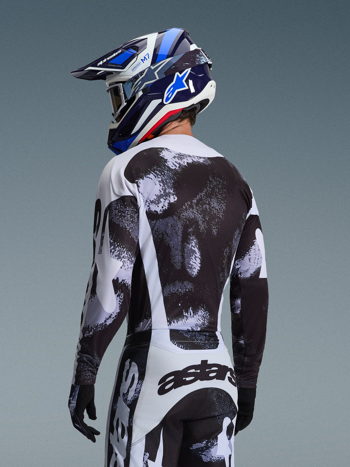 Completo Alpinestars Racer Lahnd 2026, pilota di motocross visto da dietro con maglia e pantaloni con grafica punteggiata bianco e nero, casco Alpinestars blu e bianco e guanti neri, abbigliamento tecnico per corse fuoristrada