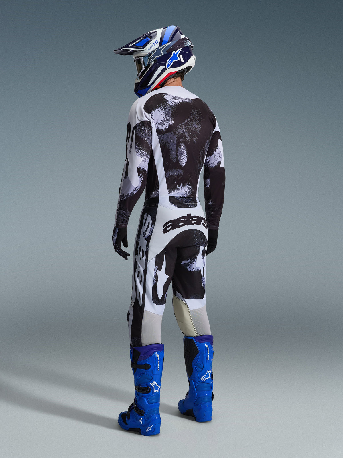 Set Gear Alpinestars Racer Lahnd 2026, vista posteriore di un pilota di motocross che indossa maglia e pantaloni con motivo astratto bianco e nero, stivali e casco blu, kit da gara professionale per prestazioni off-road