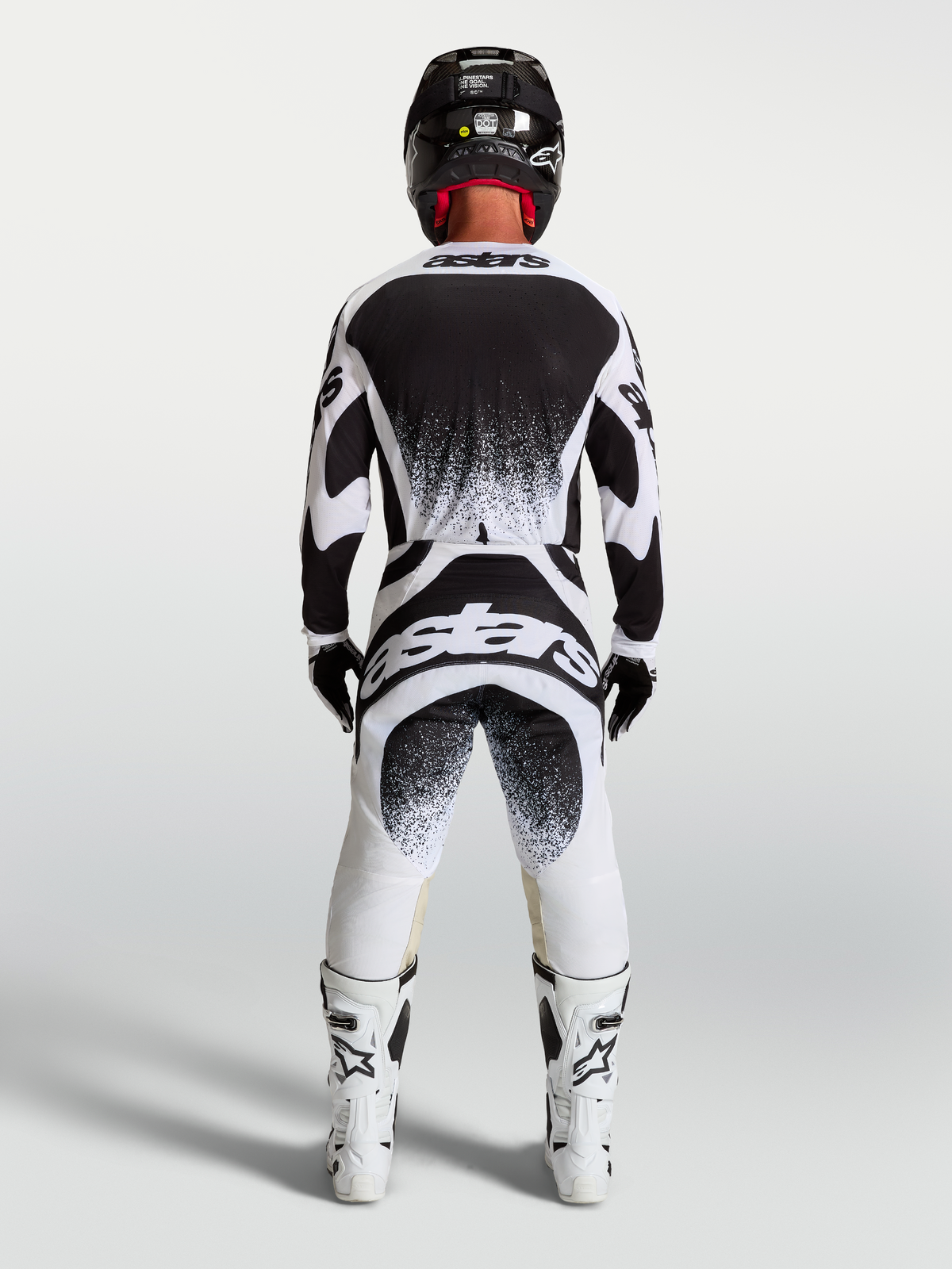 Alpinestars Maglia e Completo Techstar Swan, completo motocross da uomo, bianco e nero con grafiche splatter posteriori, vista posteriore su un pilota, abbigliamento off-road
