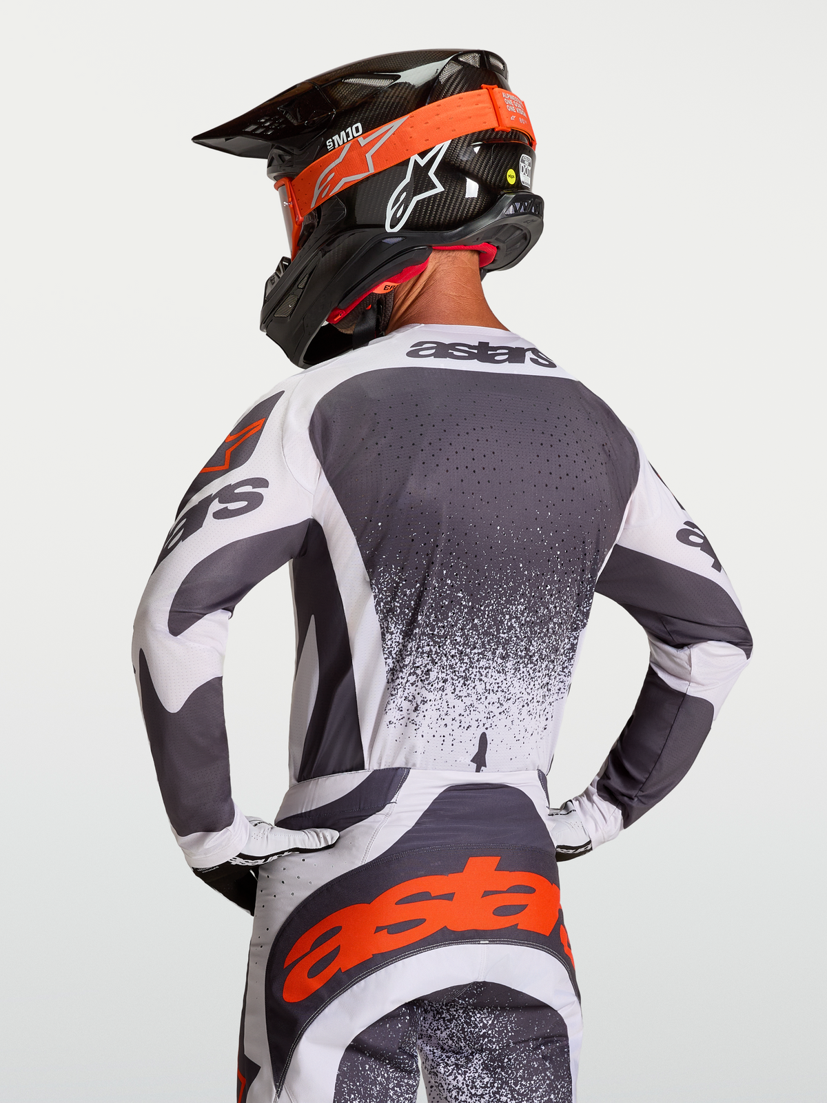 Alpinestars Maglia Techstar Swan, maglia motocross atletica da uomo, grigio scuro e bianco con dettagli rossi, vista posteriore su pilota con casco, tessuto traspirante e ventilato