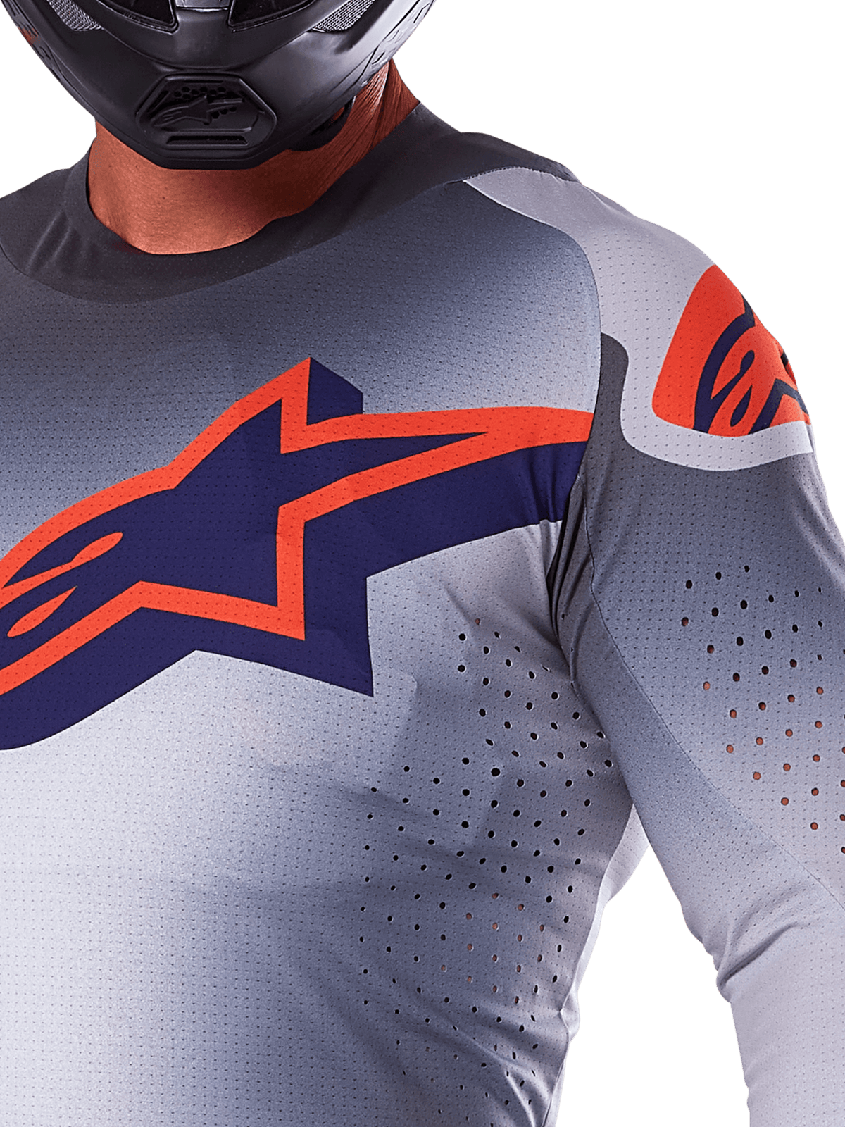 Primo piano di un pilota che indossa la maglia Alpinestars 2025 Supertech Lipan, maglia da motocross, grigio e arancione fluo, caratterizzata da un grande logo Alpinestars arancione sul petto, fori di ventilazione tagliati al laser e un casco nero, abbigliamento da gara professionale.