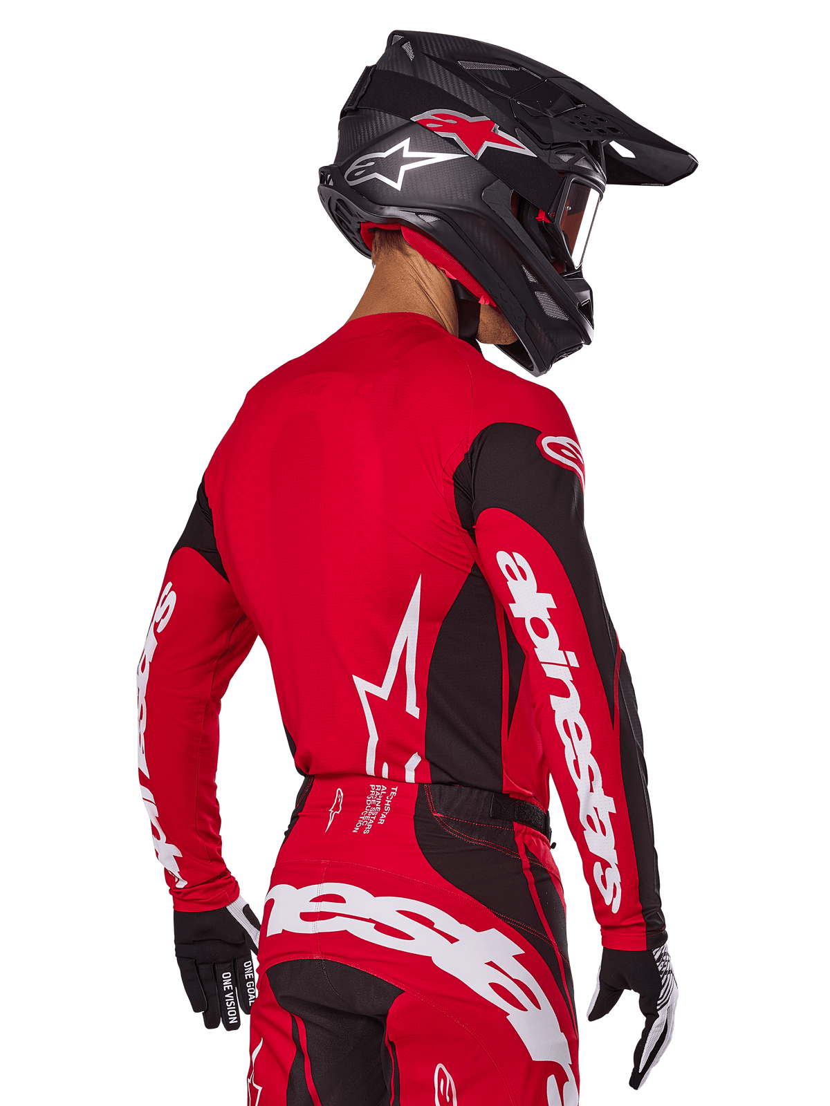 Pilota di motocross visto da dietro con completo Alpinestars Techstar Dreem 2025, maglia rossa e nera con loghi bianchi sulle maniche, pantaloni coordinati rossi e neri con logo bianco sulla seduta, casco in carbonio nero con accenti rossi, guanti bianchi e neri, abbigliamento professionale da gara fuoristrada