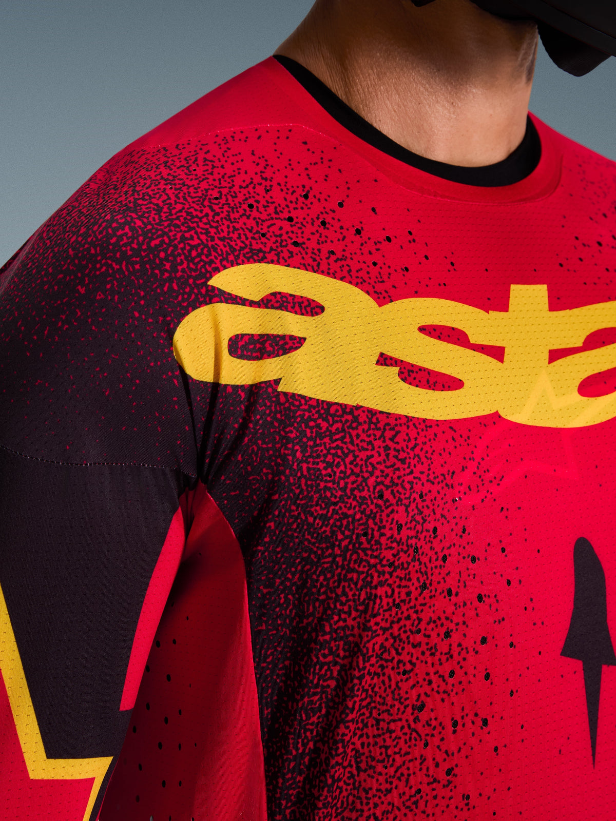 Primo piano della maglia Alpinestars Supertech Scenz 2026 in rosso, nero e giallo, con un grande logo giallo sul petto, perforazioni tagliate al laser per un maggiore flusso d'aria e una leggera texture in mesh per il motocross professionale.