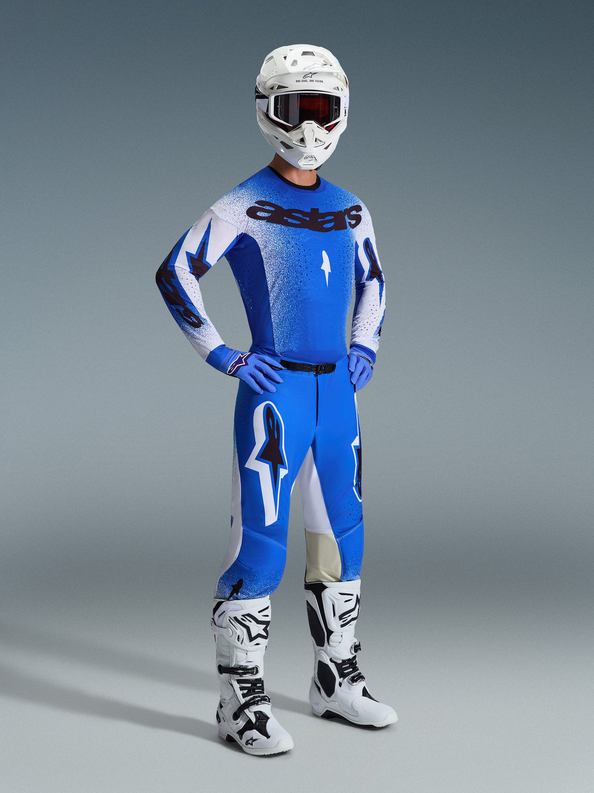 Pilota di motocross che indossa il completo Alpinestars 2026 Supertech Scenz in blu Ucla e bianco, con maglia di livello professionale con marchio 'astars', pantaloni coordinati, casco bianco, maschera scura e stivali da fuoristrada bianchi e neri.