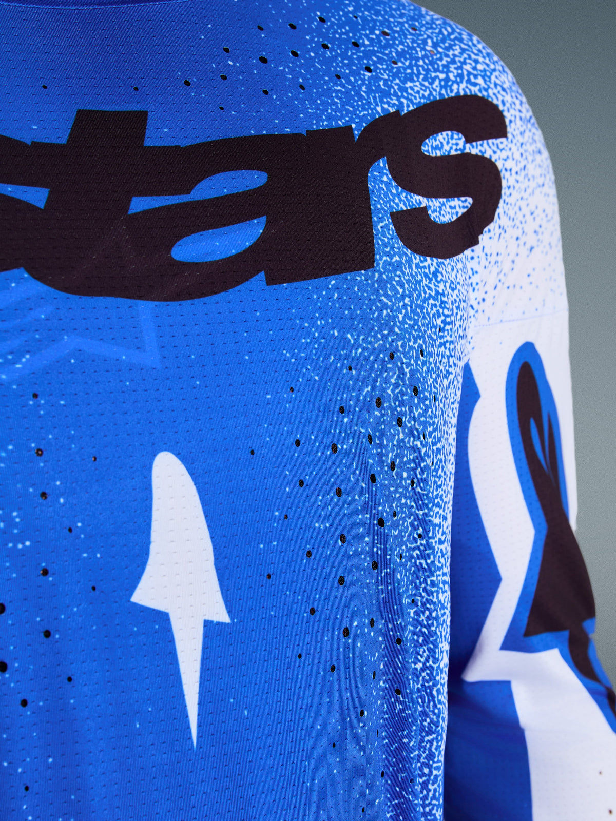 Alpinestars 2026 Supertech Scenz Jersey, primo piano del design Ucla Blue e bianco, con perforazioni tagliate al laser per la ventilazione, branding 'stars' nero e tessuto in mesh traspirante per gare di motocross professionali
