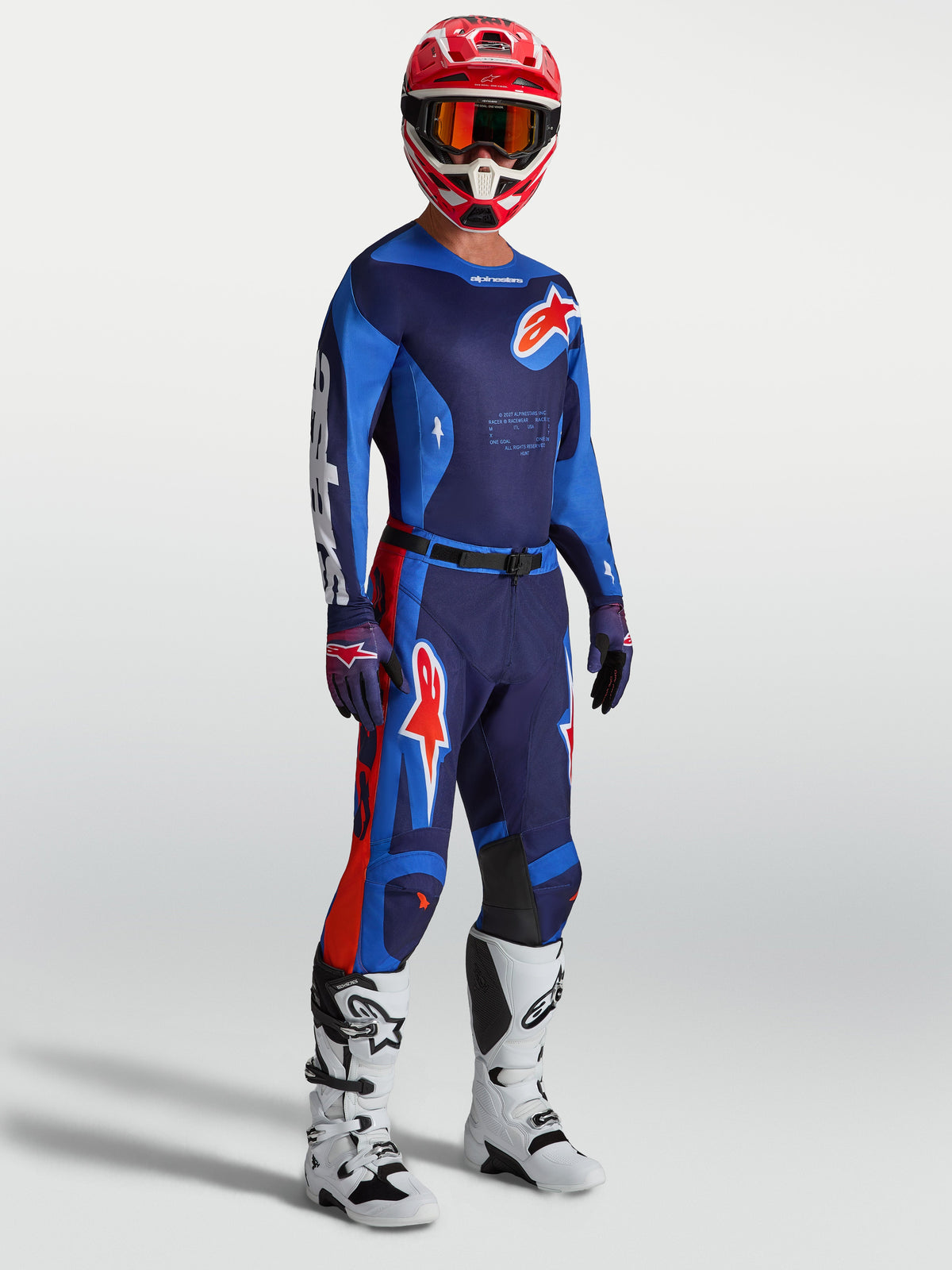 Alpinestars Completo Racer Hunt, completo da motocross blu navy e blu con dettagli rossi, stivali bianchi e casco rosso.