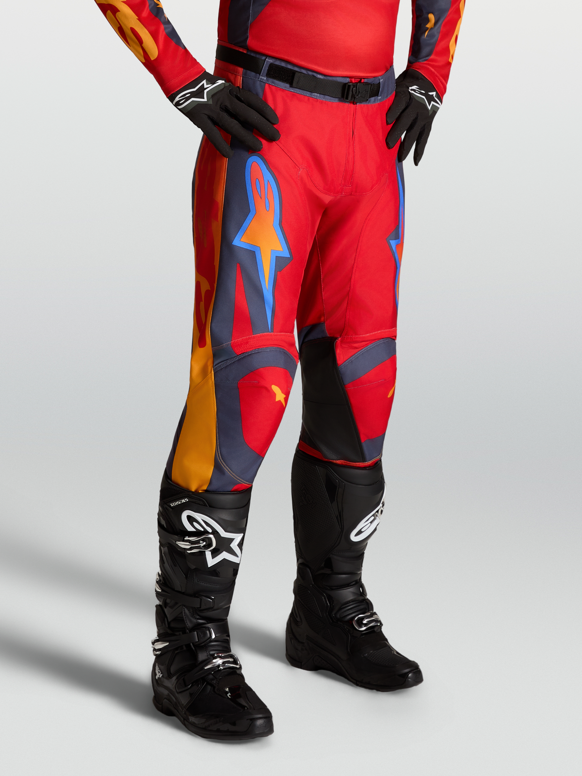 Alpinestars Pantaloni Racer Hunt, pantaloni motocross da uomo, rosso e grigio con dettagli corallo, indossati da un modello con stivali neri, certificati per prestazioni off-road.