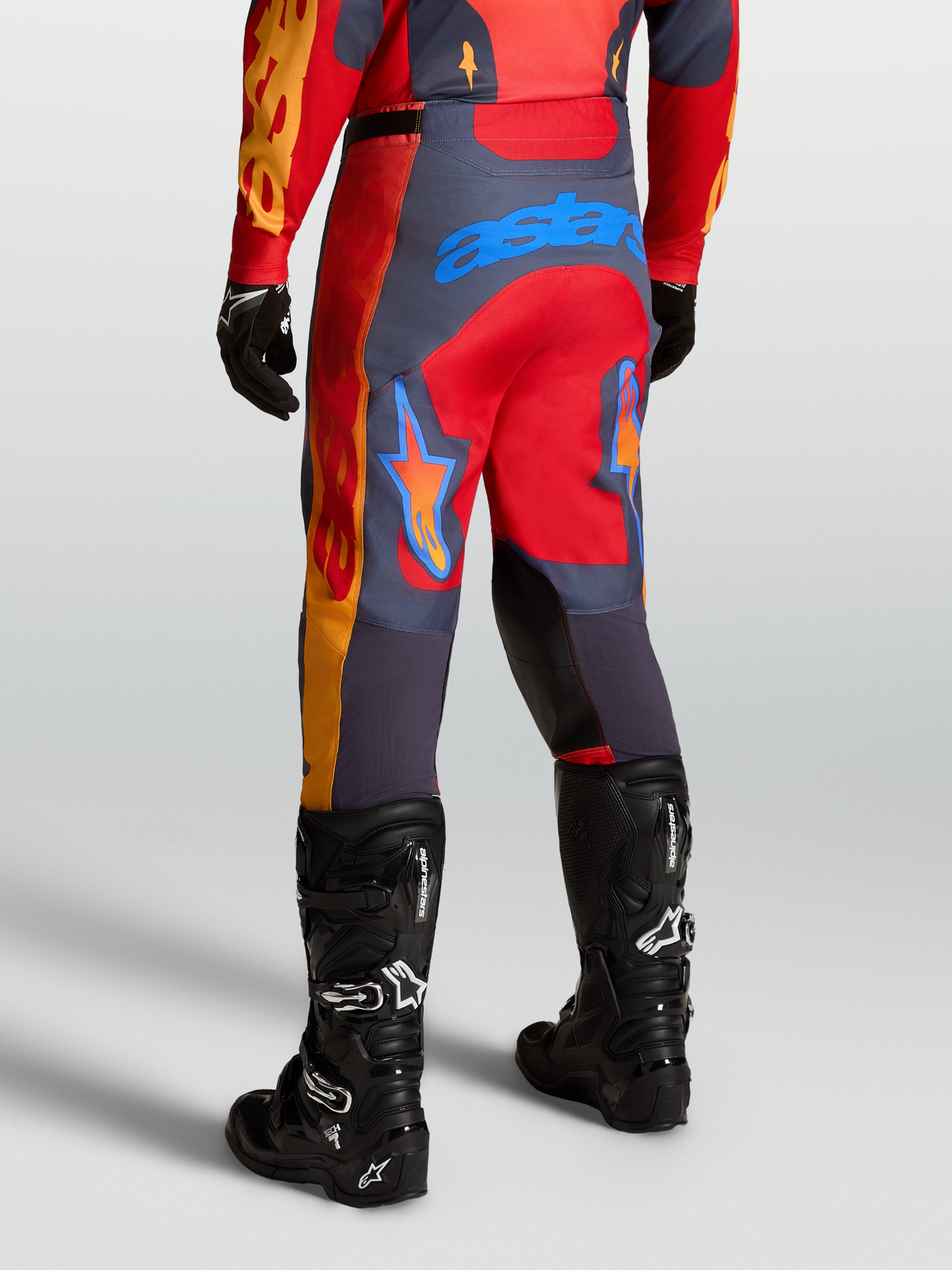 Alpinestars Pantaloni Racer Hunt, pantaloni da motocross racing in rosso fire e grigio stone, vista posteriore con stivali tecnici neri.