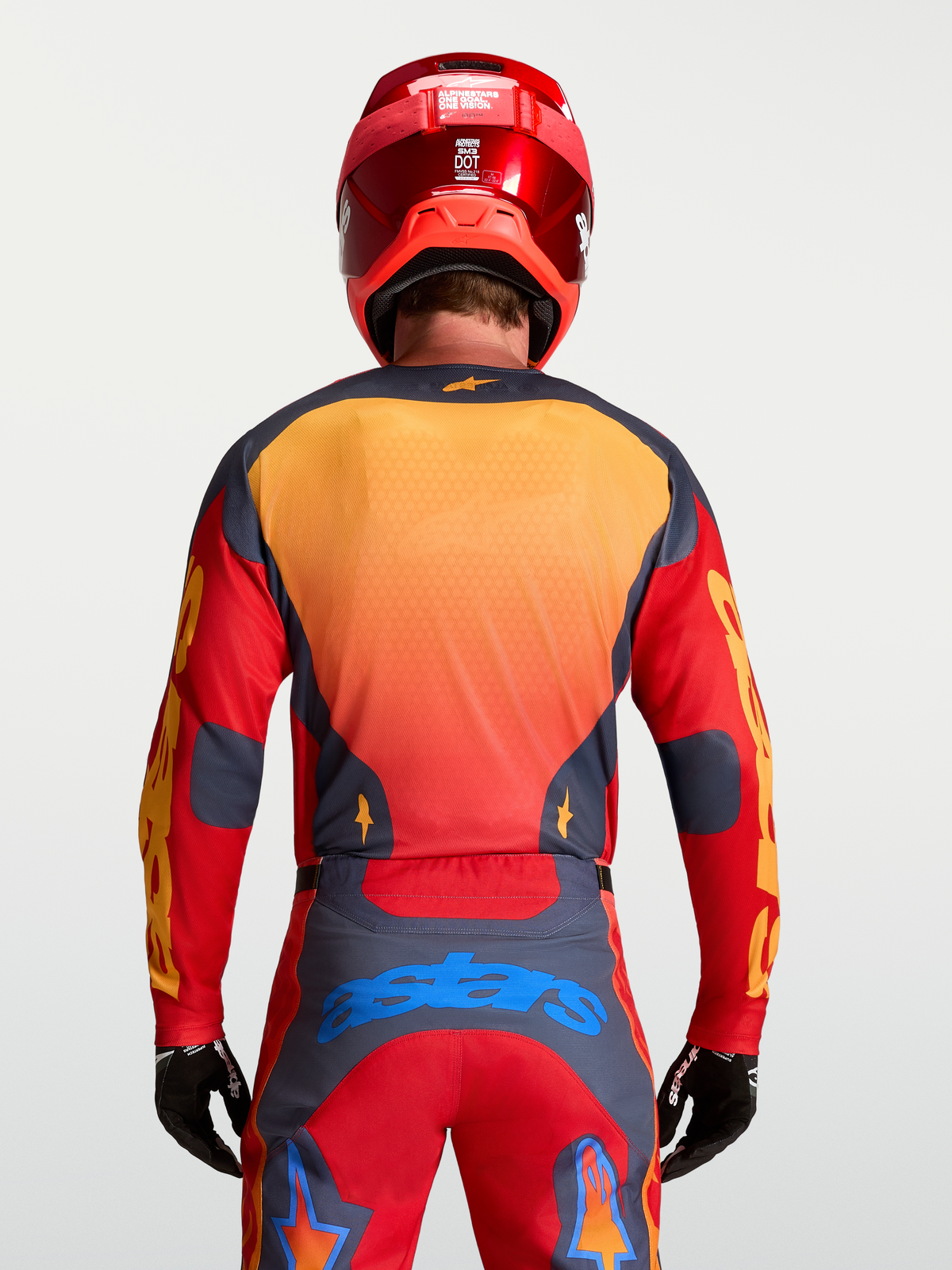 Alpinestars Maglia Racer Hunt, maglia motocross da uomo, rosso fuoco e grigio con dettagli gialli e blu, vista posteriore su modello con casco e guanti