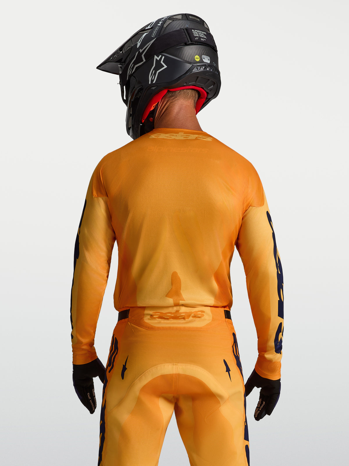 Alpinestars Maglia Racer Amber, maglia da motocross da uomo, arancione e dorata, con pannelli in mesh traspiranti e taglio posteriore allungato, vista posteriore su modello.