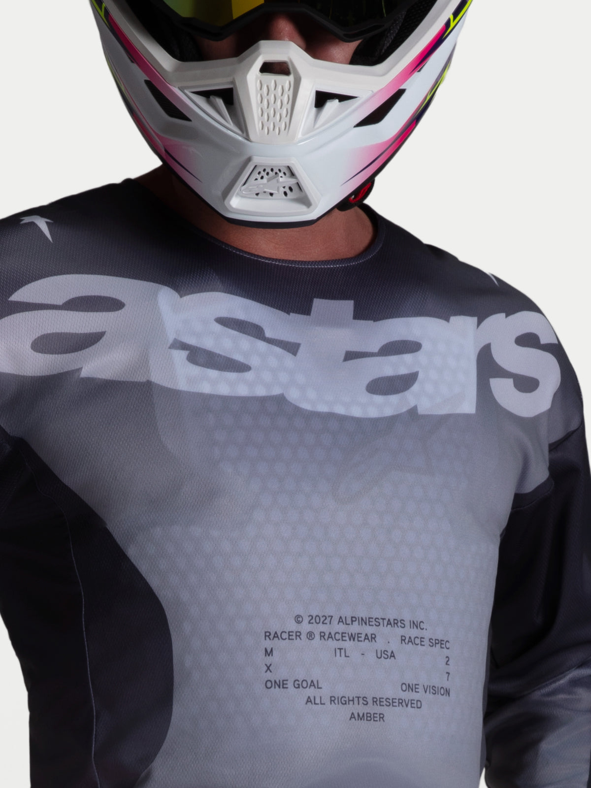 Alpinestars Maglia Racer Amber, maglia da motocross da uomo, grigio e nero, con grande logo astars sul petto, in polyfabric traspirante con pannelli in mesh, indossata con casco da motocross bianco e rosa