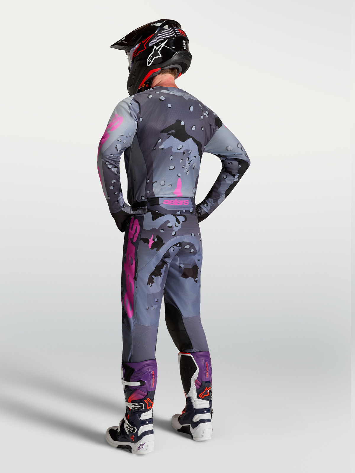 Alpinestars Pantaloni Racer Lone, pantaloni da motocross da uomo, grigio camo e viola, vista posteriore con maglia e stivali.