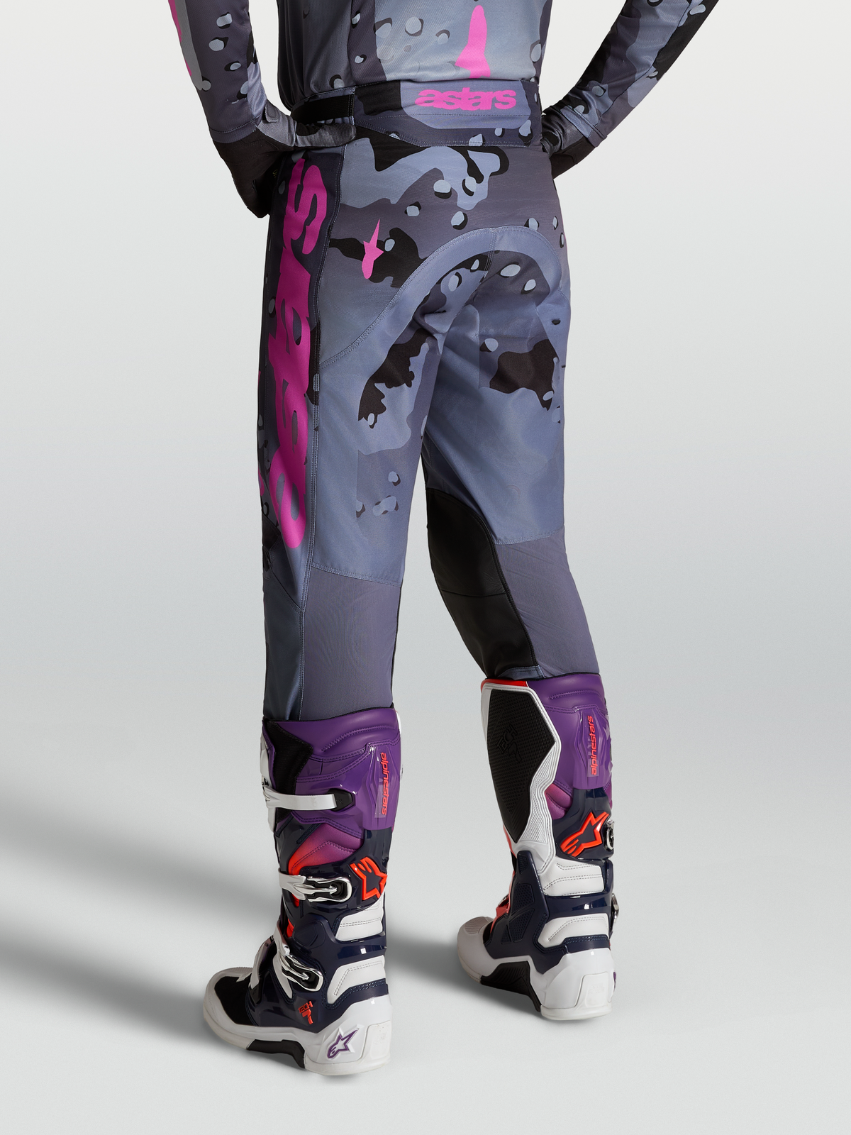 Alpinestars Pantaloni Racer Lone, pantaloni da motocross grigio camo e viola, vista posteriore su modello con stivali Tech 7.