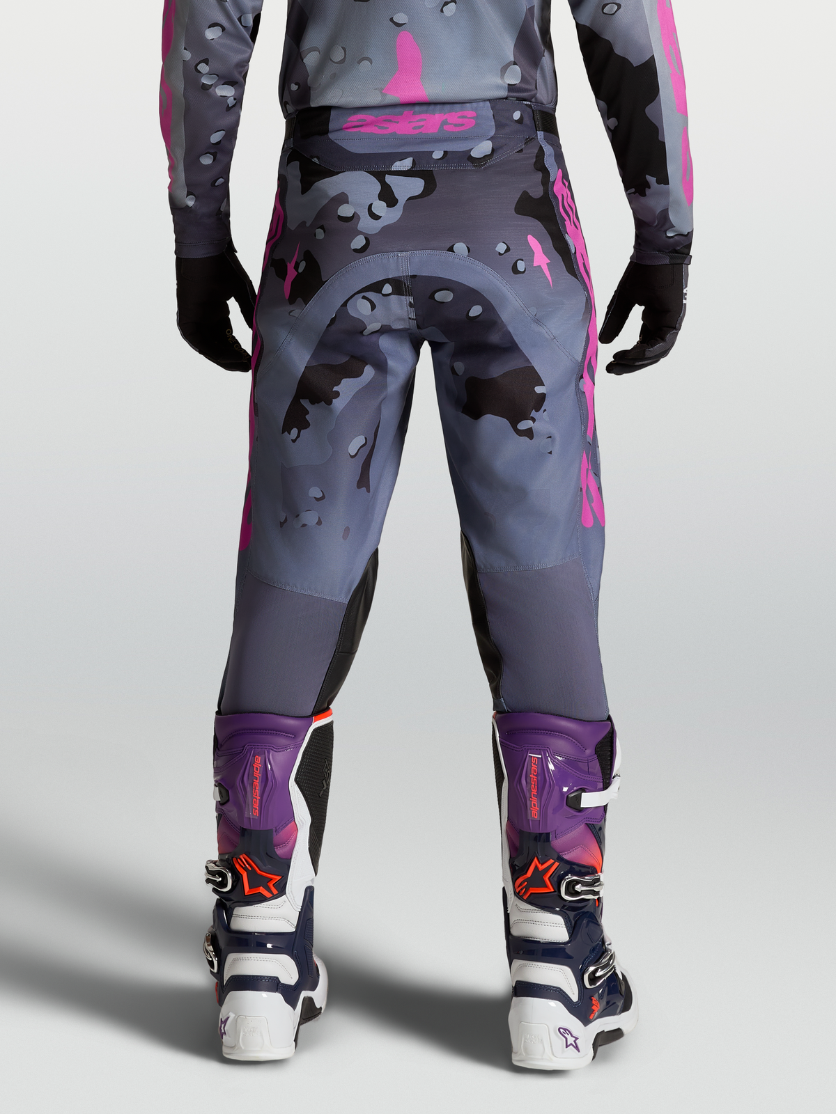 Alpinestars Pantaloni Racer Lone, pantaloni motocross da uomo, grigio e viola camo, vista posteriore su modello con stivali MX coordinati, design fuoristrada durevole.