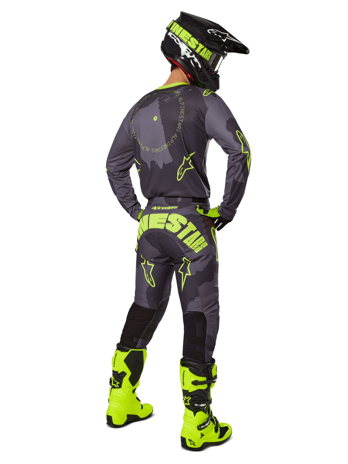 Vista posteriore di un pilota di motocross con il set completo Alpinestars Racer Hollow 2025 in Dark Camo Giallo Fluo, maglia camo grigia con dettagli giallo fluo, pantaloni coordinati con logo evidente sul retro, stivali giallo fluo e casco nero con maschera gialla.