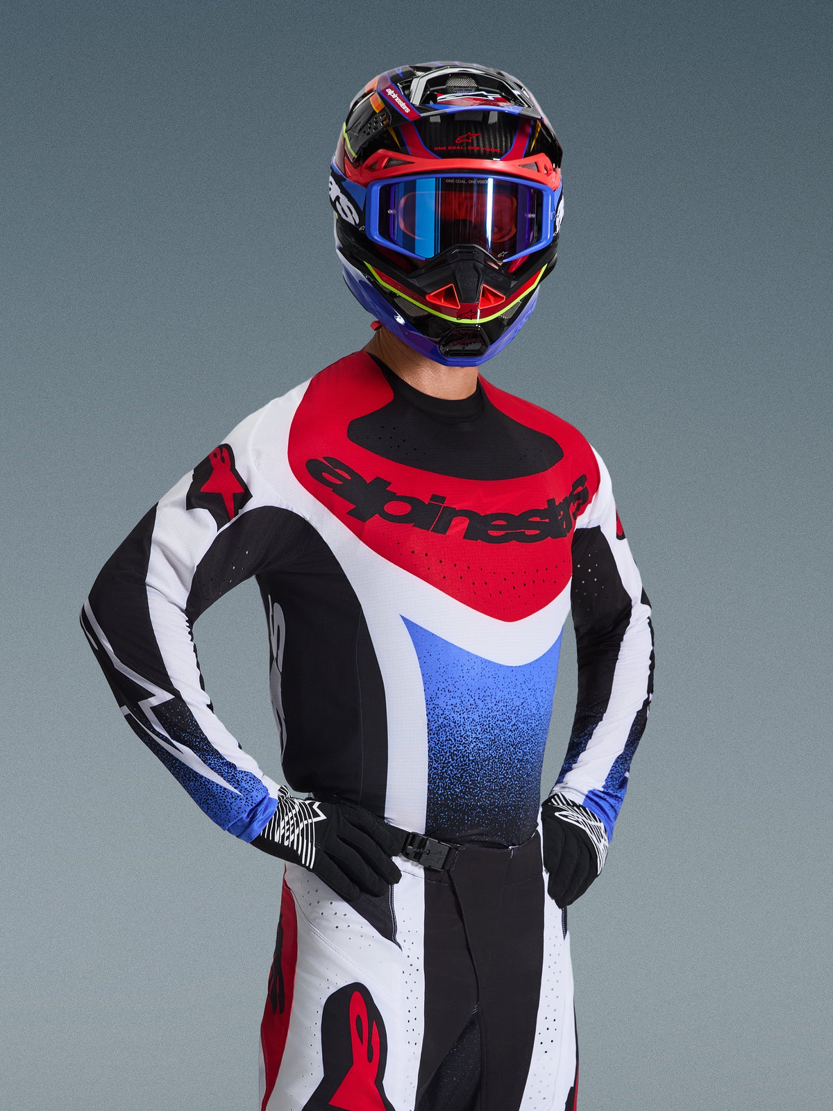 Pilota di motocross che indossa la maglia Alpinestars Techstar Knif 2026 in rosso, bianco e blu, con marchio nero sul petto, abbinata a pantaloni da motocross coordinati, casco da corsa con occhiali blu e guanti neri e bianchi, attrezzatura professionale da fuoristrada per competizioni
