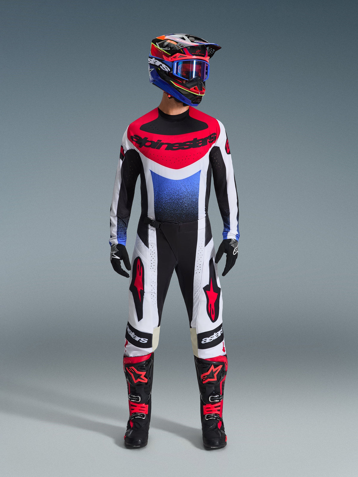Alpinestars 2026 Techstar Knif Jersey, maglia da motocross in bianco, nero, rosso e blu con grafica sfumata blu, indossata come parte di un kit da gara off-road completo con pantaloni abbinati, stivali neri e rossi e casco coordinato con occhiali.
