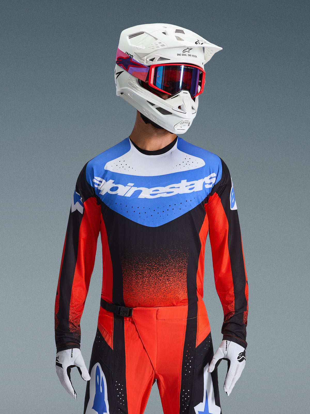 Set completo Alpinestars Techstar Knif 2026, abbigliamento da gara per motocross con maglia blu, bianca, nera e rossa con marchio Alpinestars, pantaloni coordinati rossi e neri, indossato con casco bianco, occhiali rossi e guanti bianchi, vestibilità atletica per competizioni off-road